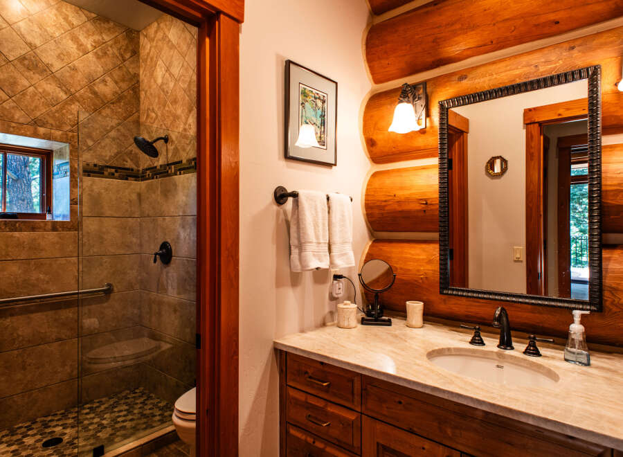 Experience rustic charm in this log cabin bathroom, featuring a spacious tiled shower with a rainfall showerhead and a convenient grab bar.