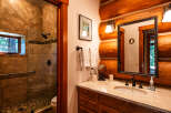 Experience rustic charm in this log cabin bathroom, featuring a spacious tiled shower with a rainfall showerhead and a convenient grab bar.