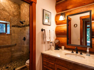 Experience rustic charm in this log cabin bathroom, featuring a spacious tiled shower with a rainfall showerhead and a convenient grab bar.