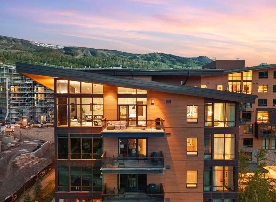 Experience luxury mountain living in this stunning modern residence, featuring expansive floor-to-ceiling windows that showcase breathtaking panoramic views of the surrounding peaks and vibrant sunset skies.