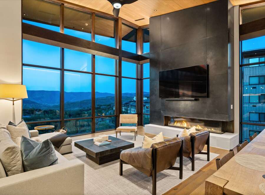 Experience luxury living with this stunning modern living room, featuring a grand fireplace and floor-to-ceiling windows that offer breathtaking mountain views.
