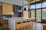 Experience modern luxury in this stunning kitchen, featuring sleek wood cabinetry, a spacious quartz island with bar seating, and a dramatic black range hood.