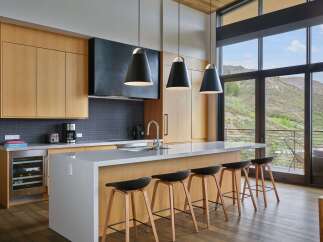 Experience modern luxury in this stunning kitchen, featuring sleek wood cabinetry, a spacious quartz island with bar seating, and a dramatic black range hood.