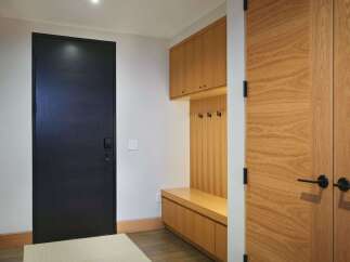 Step into a modern entryway featuring a sleek black door and warm wood accents.