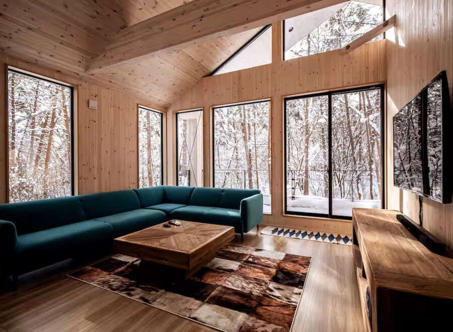 Experience serene winter living in this modern cabin featuring a spacious sectional sofa and a rustic wooden coffee table.