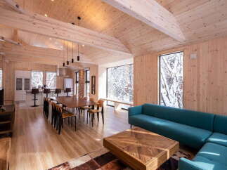 Experience modern living in this stunning open-concept space, featuring a vaulted wood-paneled ceiling and expansive windows showcasing a serene winter landscape.