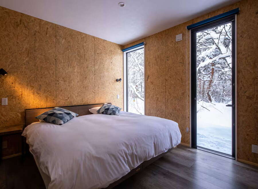 Experience cozy winter living in this unique bedroom, featuring rustic OSB walls and a comfortable bed.