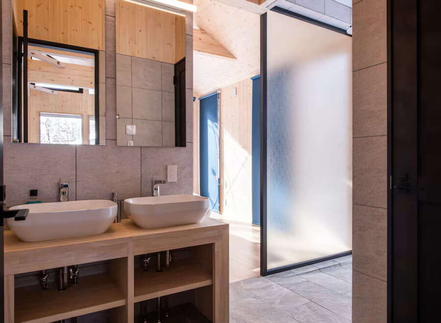 Experience modern luxury in this stunning bathroom featuring dual vessel sinks atop a sleek wooden vanity.