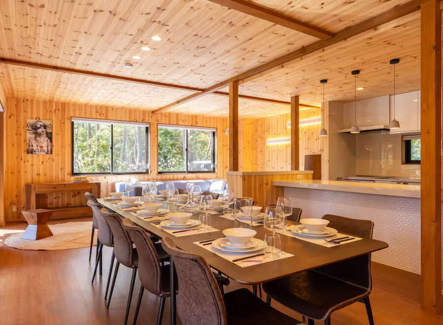 Experience the warmth of natural wood in this stunning dining area, featuring a long wooden table set for a feast.
