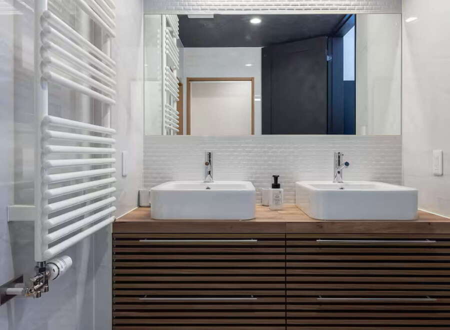Experience modern luxury in this stunning bathroom featuring a sleek wooden vanity with dual vessel sinks and chrome fixtures.