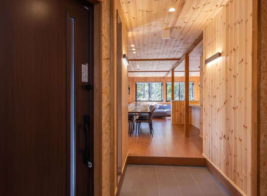 Step into this inviting entryway featuring a rich brown door and a textured doormat, leading to a hallway with warm wood paneling and modern lighting.