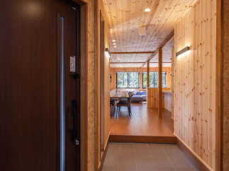 Step into this inviting entryway featuring a rich brown door and a textured doormat, leading to a hallway with warm wood paneling and modern lighting.
