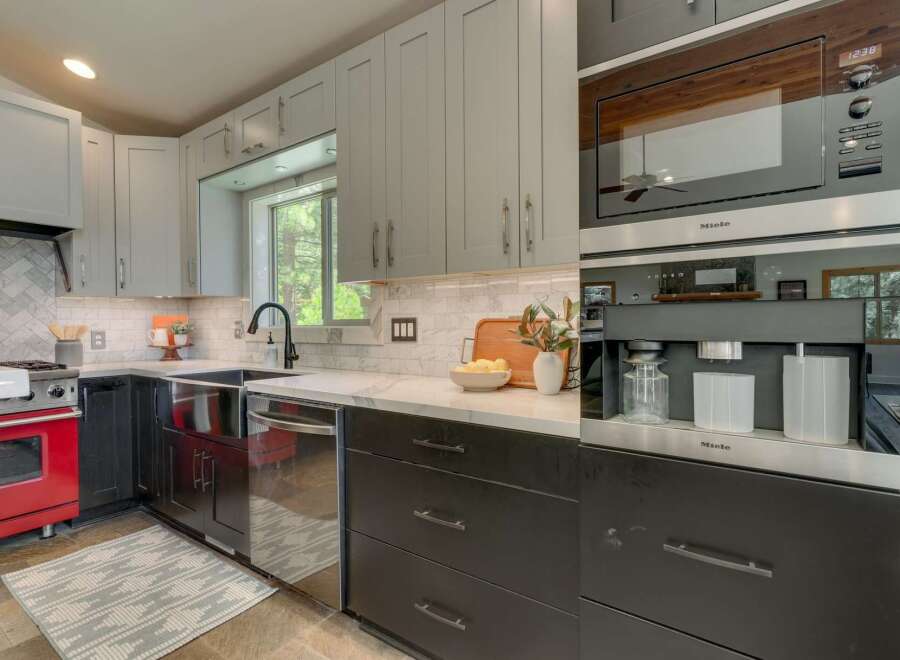 This modern kitchen boasts sleek gray cabinetry, a striking red gas range, and a built-in Miele coffee system.