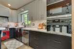 This modern kitchen boasts sleek gray cabinetry, a striking red gas range, and a built-in Miele coffee system.