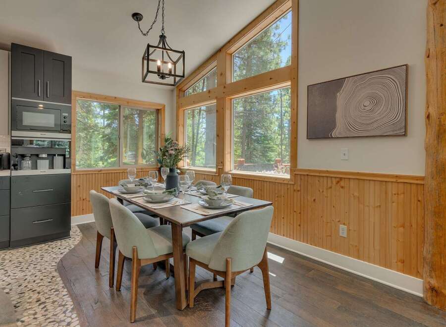 Experience dining amidst nature in this stunning home, featuring a spacious dining area with large windows that offer breathtaking forest views.