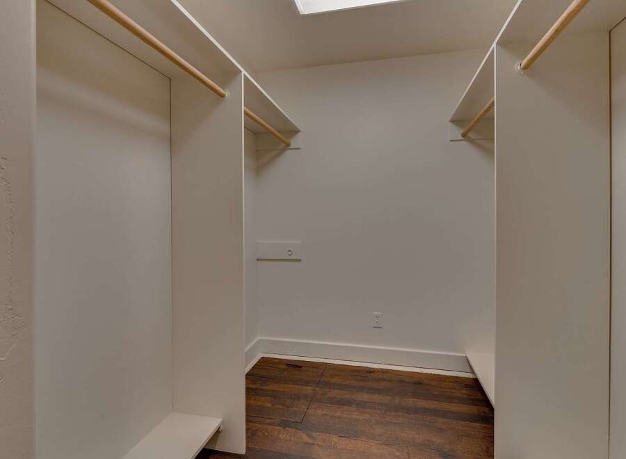 Step into this spacious walk-in closet, featuring ample hanging space with natural wood rods and built-in shelving.