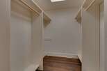 Step into this spacious walk-in closet, featuring ample hanging space with natural wood rods and built-in shelving.