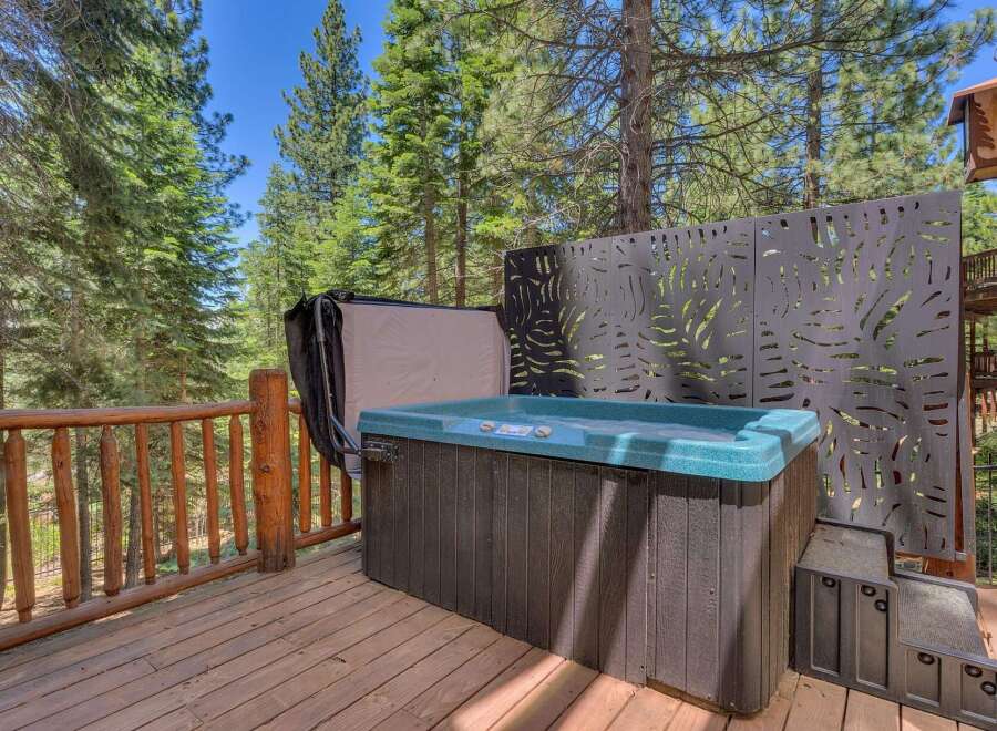 Enjoy ultimate relaxation in this luxurious hot tub, perfectly situated on a spacious wooden deck surrounded by the serene beauty of tall pine trees.