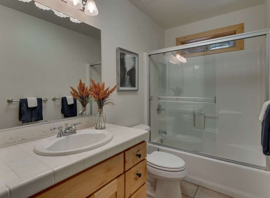 This charming bathroom features a spacious vanity with a tiled countertop and a white undermount sink, complemented by warm wood cabinetry.