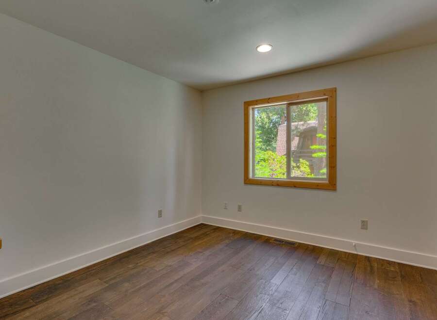 This bright and airy room features a large window with a wooden frame, offering picturesque views of the surrounding greenery and a charming house.