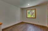 This bright and airy room features a large window with a wooden frame, offering picturesque views of the surrounding greenery and a charming house.