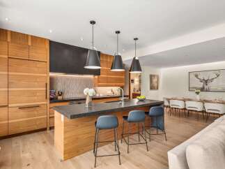 Experience modern luxury in this stunning kitchen featuring sleek, custom wood cabinetry and a spacious waterfall island with a dark stone countertop.