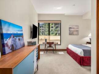 This modern bedroom features a comfortable queen-size bed with a plush red velvet headboard, complemented by a sleek wooden dresser and a wall-mounted television.