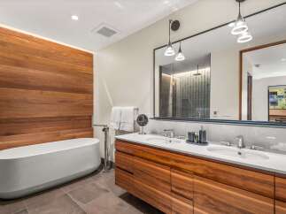 Experience modern luxury in this stunning bathroom, featuring a sleek freestanding bathtub set against a warm, wood-paneled accent wall.