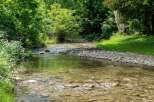 Discover serene living with this charming property, featuring a picturesque stream flowing through lush greenery.