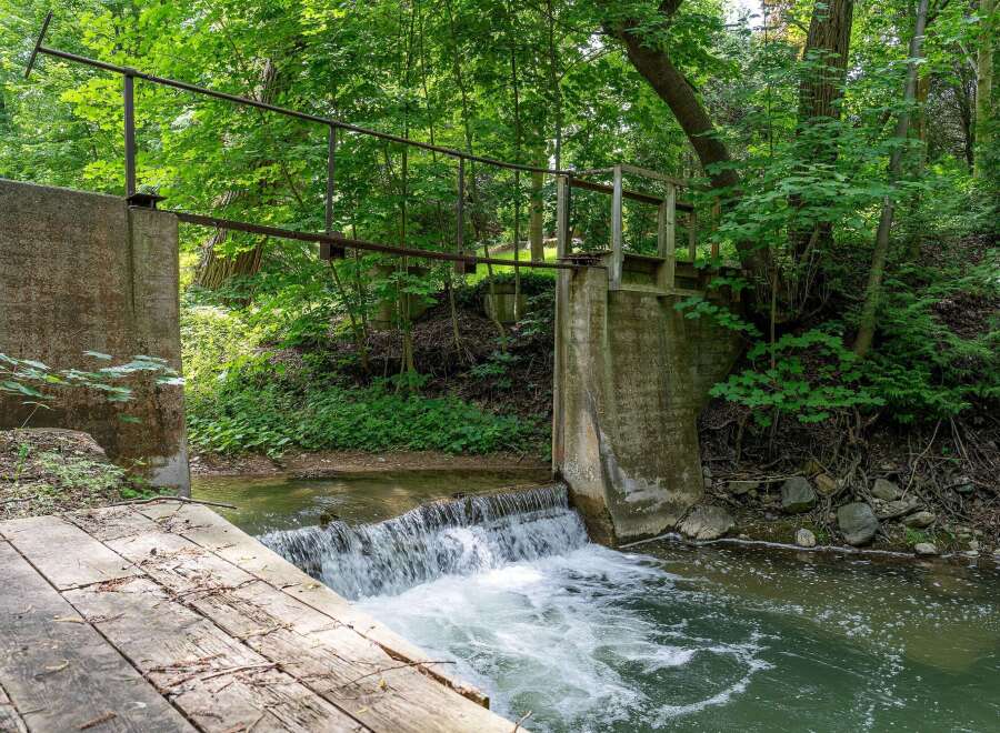 Discover a serene natural escape with this charming property featuring a picturesque waterfall and a rustic wooden bridge.
