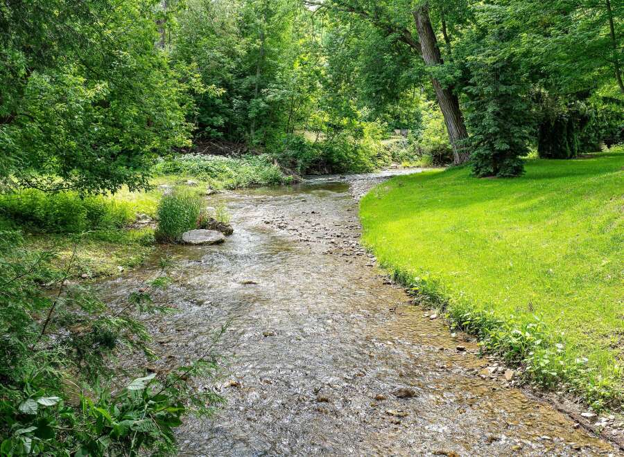 Discover a serene retreat with this charming property, featuring a picturesque stream flowing through lush greenery.