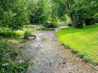 Discover a serene retreat with this charming property, featuring a picturesque stream flowing through lush greenery.