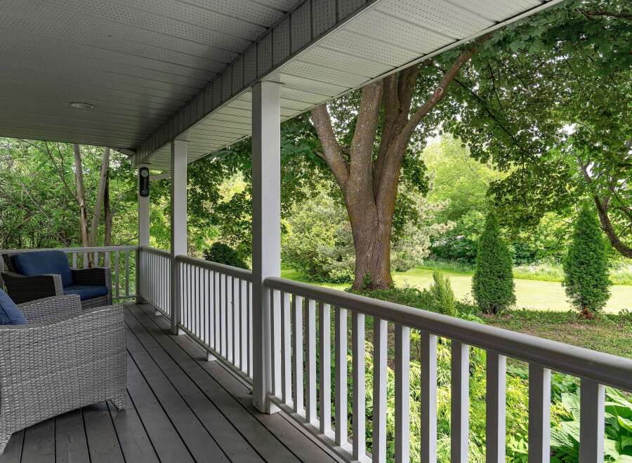 Enjoy the serene outdoors from this charming covered porch, featuring comfortable wicker seating and a picturesque view of lush greenery.