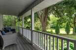 Enjoy the serene outdoors from this charming covered porch, featuring comfortable wicker seating and a picturesque view of lush greenery.