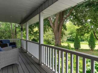 Enjoy the serene outdoors from this charming covered porch, featuring comfortable wicker seating and a picturesque view of lush greenery.