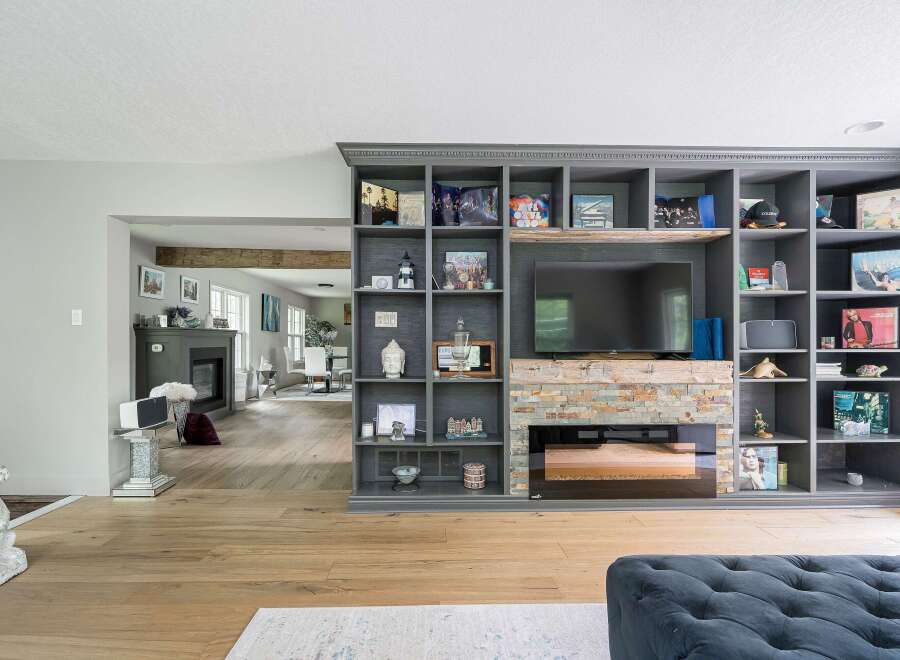 This living room features a large, built-in gray bookshelf unit that houses a television and a fireplace with a stacked stone surround.