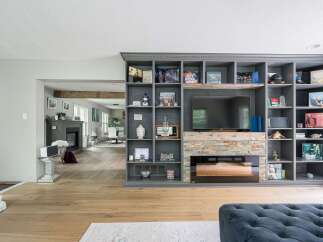 This living room features a large, built-in gray bookshelf unit that houses a television and a fireplace with a stacked stone surround.