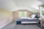Discover comfort and style in this charming bedroom, featuring a plush grey comforter on a queen-sized bed and a sophisticated tufted blue ottoman.