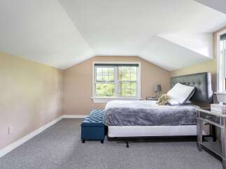 Discover comfort and style in this charming bedroom, featuring a plush grey comforter on a queen-sized bed and a sophisticated tufted blue ottoman.