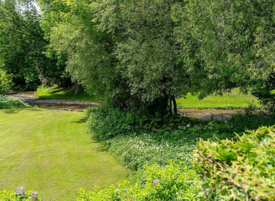Experience serene living with this picturesque property featuring a lush green lawn leading to a tranquil stream.
