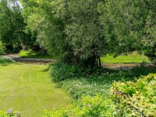 Experience serene living with this picturesque property featuring a lush green lawn leading to a tranquil stream.