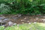 Escape to nature with this serene property featuring a tranquil stream flowing through lush greenery.