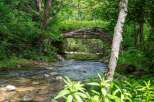Discover a serene natural escape with this picturesque property featuring a charming creek flowing under a rustic bridge.