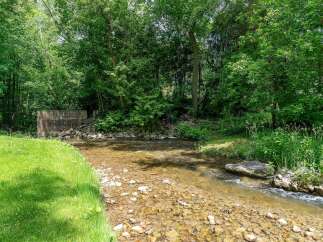 Escape to nature with this serene property featuring a charming creek flowing through lush greenery.
