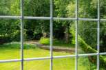 Experience serene living with this picturesque view of a babbling brook and lush greenery, framed by a charming window grid.