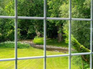 Experience serene living with this picturesque view of a babbling brook and lush greenery, framed by a charming window grid.
