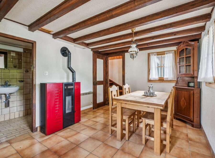 Experience rustic charm in this cozy dining area featuring exposed wooden beams and a vibrant red pellet stove for warmth.
