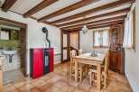 Experience rustic charm in this cozy dining area featuring exposed wooden beams and a vibrant red pellet stove for warmth.