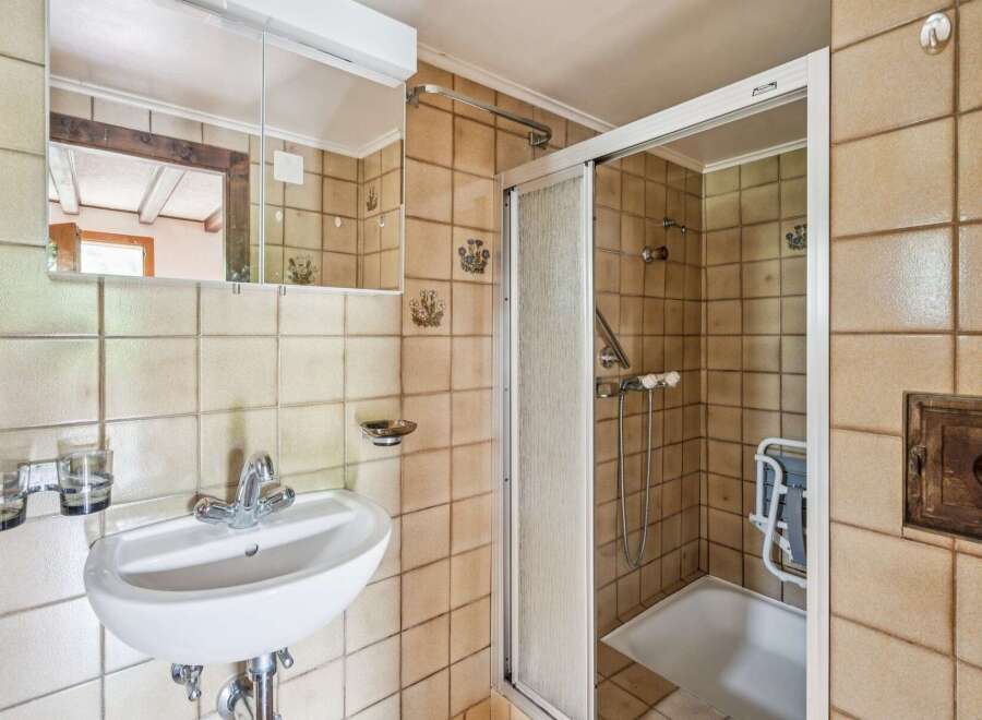 This charming bathroom features a classic tiled design with a functional shower-tub combination and a convenient vanity with a mirror.