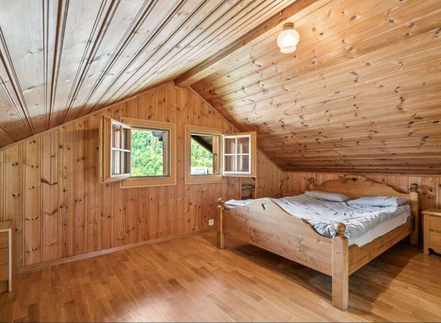 Experience rustic charm in this cozy attic bedroom, featuring warm wooden paneling throughout the walls and ceiling.